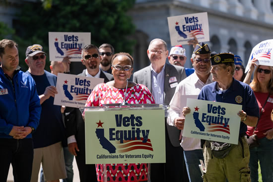 Asm. Wilson at podium in front of State Capitol, speaking, with many vets standing in support